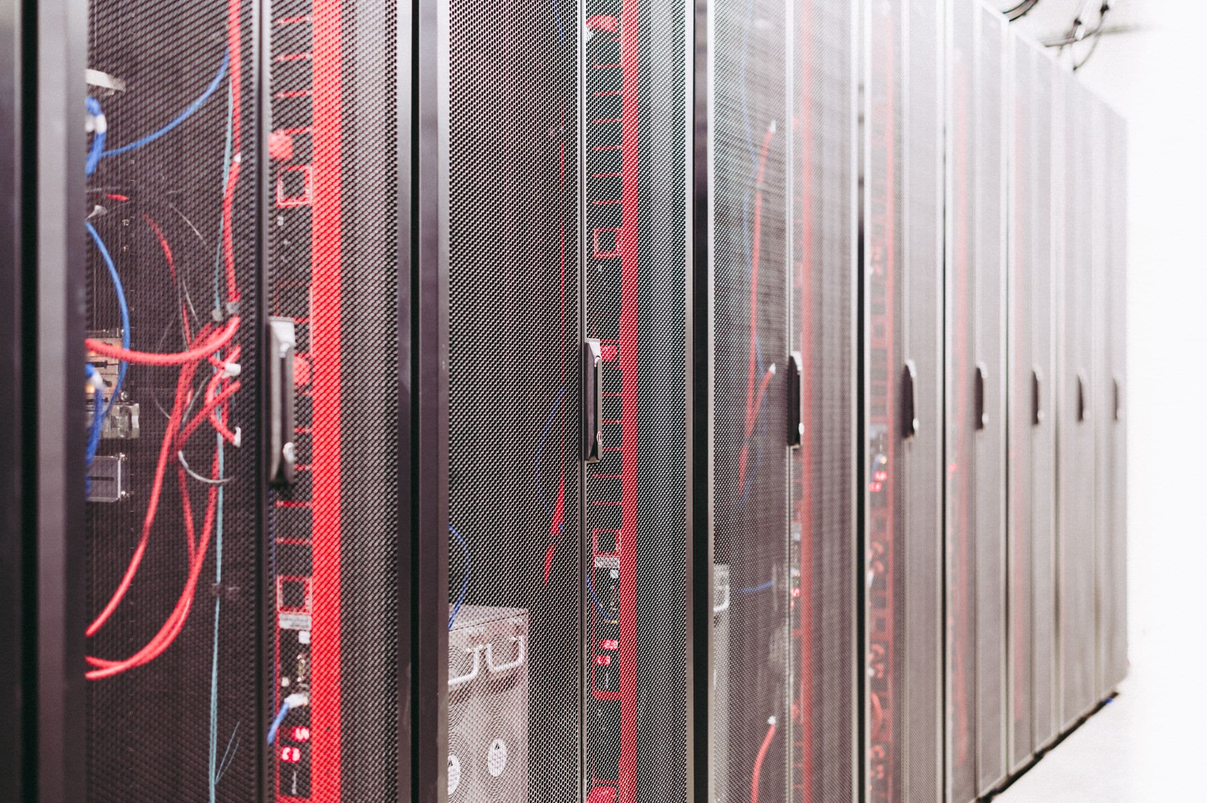 Row of enclosed server cabinets with red patch cables on a datacenter floor.