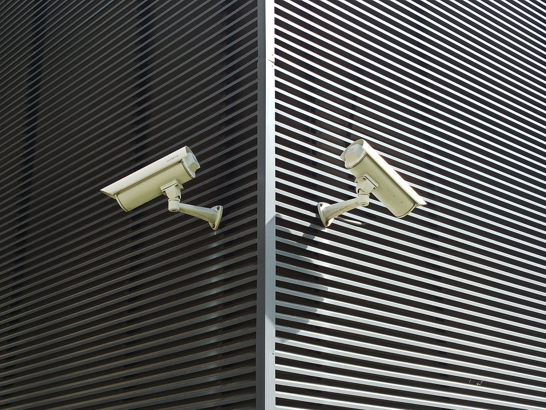 Two security cameras mounted on a slatted exterior wall.
